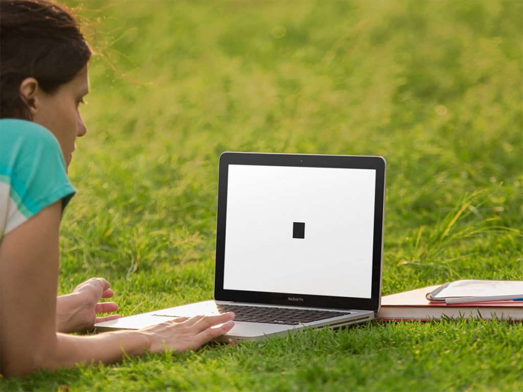 Black square on a white background displayed on a laptop on a lawn, viewed by a young woman.