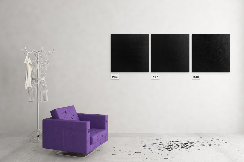 Three numbered black canvases on a wall, with black paint spattered below on the floor and a nearby chair.